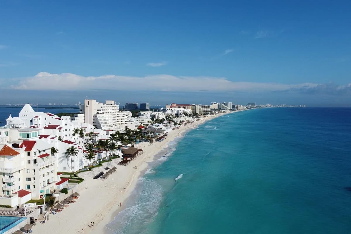 Aerial view of the hotel-lined Cancún coastline, white resort buildings between the lagoon and turquoise Caribbean water