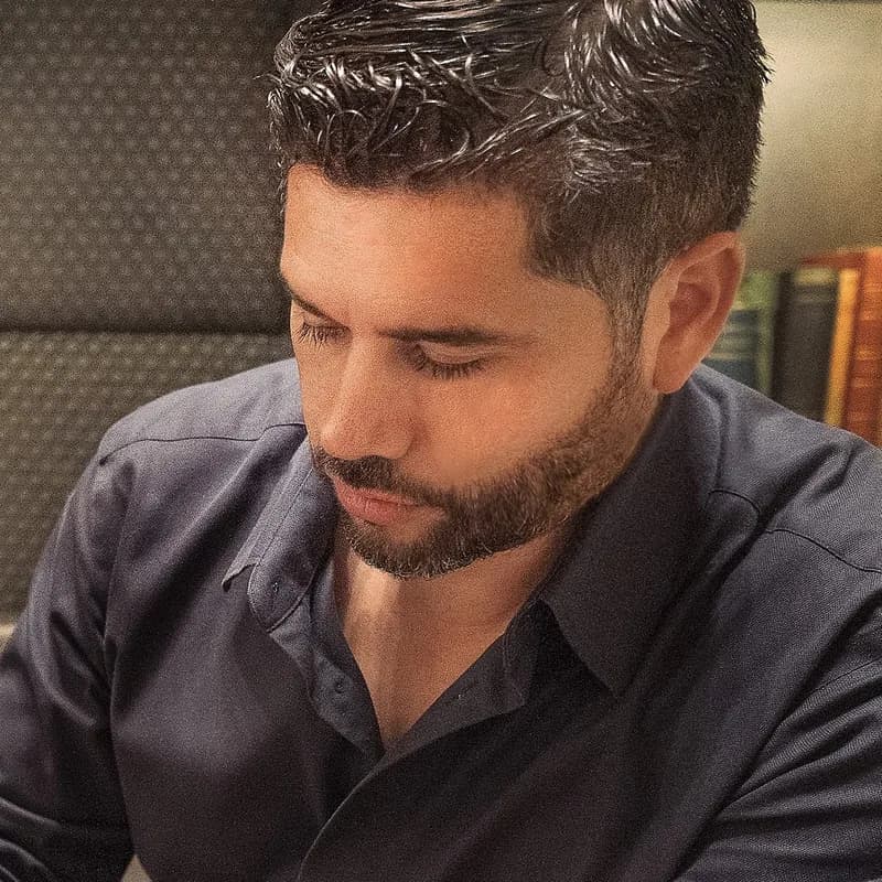A man with a short beard looking down at a camera he holds.
